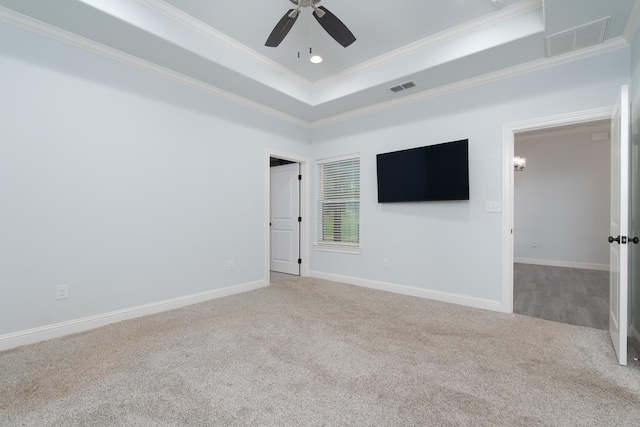 carpeted empty room with crown molding, visible vents, ceiling fan, and a tray ceiling
