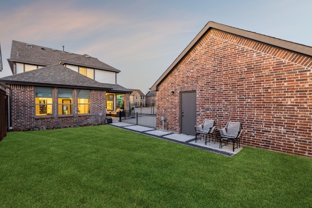 rear view of property featuring a lawn, brick siding, fence, and a patio area