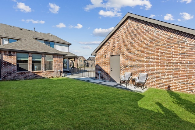 rear view of property with roof with shingles, a patio area, brick siding, and a yard