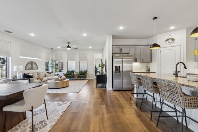 kitchen featuring stainless steel fridge with ice dispenser, gray cabinetry, a breakfast bar, dark wood-style floors, and a ceiling fan