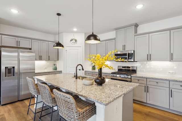 kitchen featuring a sink, light stone countertops, wood finished floors, gray cabinetry, and stainless steel appliances