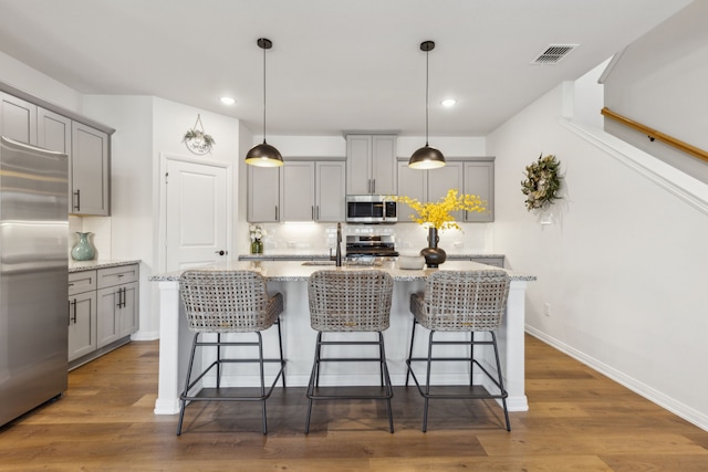 kitchen with tasteful backsplash, gray cabinets, stainless steel appliances, a breakfast bar, and visible vents
