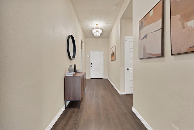 corridor with dark wood-style floors, baseboards, and a chandelier