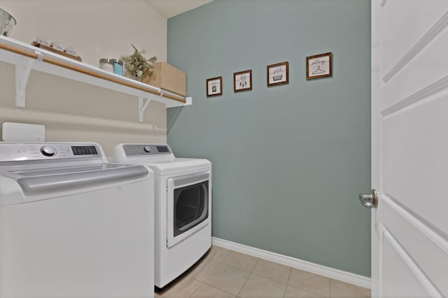 clothes washing area with laundry area, light tile patterned floors, separate washer and dryer, and baseboards