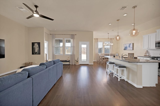 living room featuring dark wood-style floors, visible vents, ceiling fan with notable chandelier, and baseboards