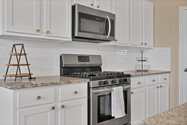 kitchen with light stone counters, backsplash, appliances with stainless steel finishes, and white cabinets