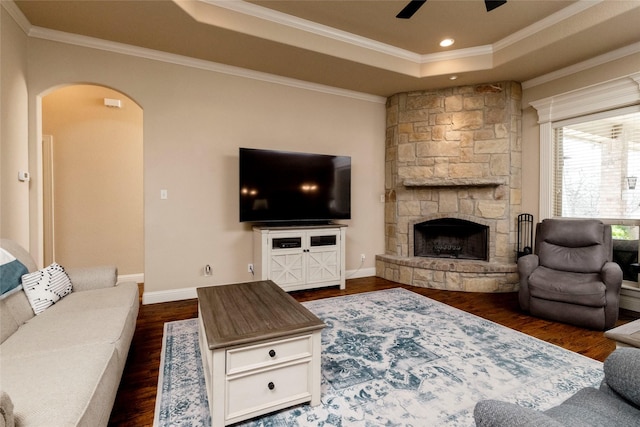 living room with ceiling fan, a raised ceiling, arched walkways, dark wood finished floors, and ornamental molding