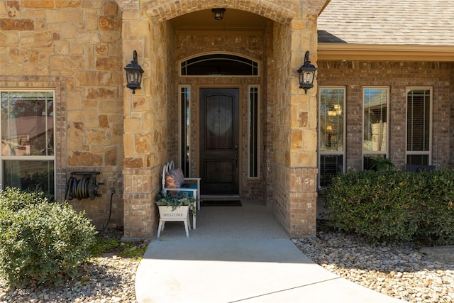 view of exterior entry with roof with shingles and stone siding