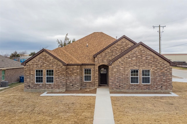view of front of house with a front yard, central AC unit, brick siding, and roof with shingles