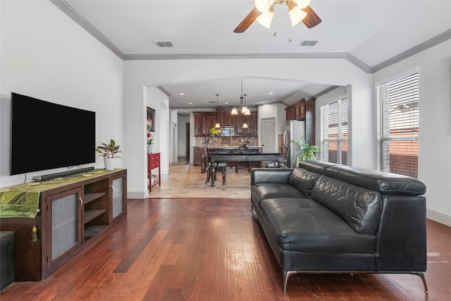 living area featuring crown molding, a ceiling fan, visible vents, and dark wood finished floors