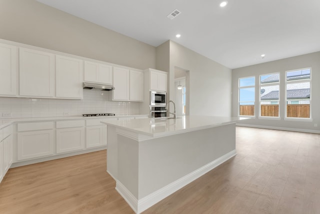 9828 Palermo Ln, Mesquite, TX 75126 - kitchen featuring visible vents, tasteful backsplash, stainless steel microwave, light wood finished floors, and under cabinet range hood