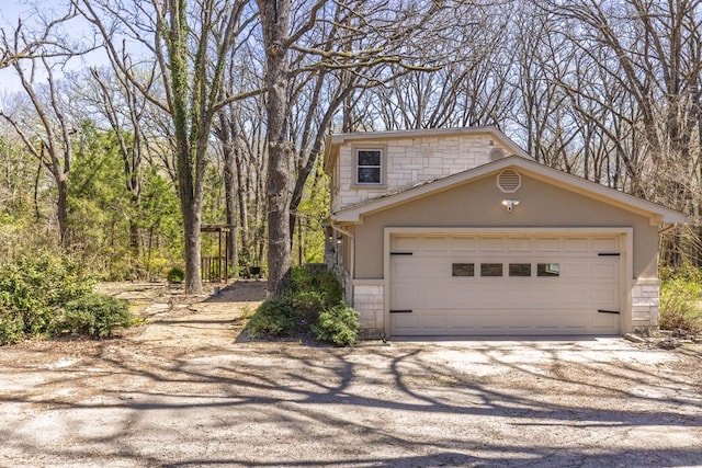 view of front of property featuring a garage, stone siding, and gravel driveway
