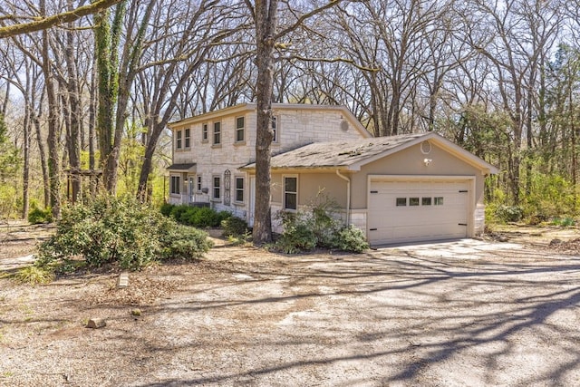 colonial-style house featuring a garage, stone siding, driveway, and stucco siding