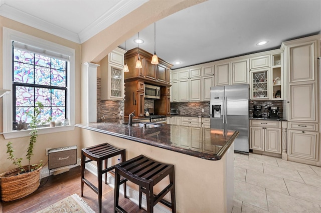 4001 Roswell St, Dallas, TX 75219 - kitchen featuring appliances with stainless steel finishes, a sink, a breakfast bar, cream cabinetry, and tasteful backsplash