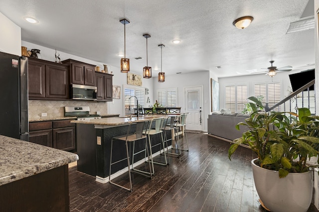 1753 Rio Penasco Rd, Fort Worth, TX 76052 - kitchen with appliances with stainless steel finishes, healthy amount of natural light, a kitchen bar, dark brown cabinetry, and a textured ceiling