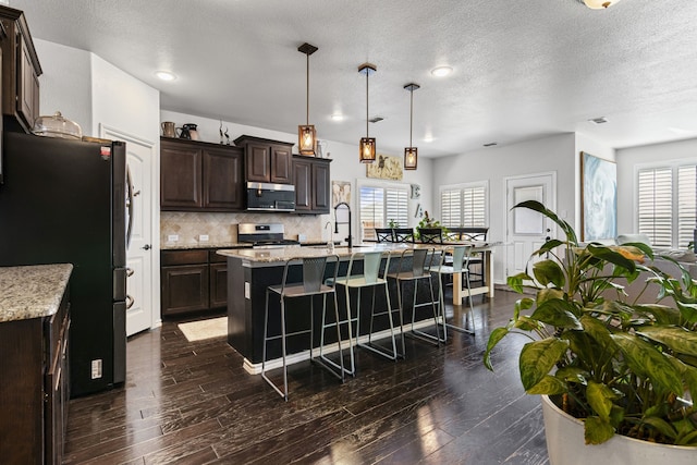 1753 Rio Penasco Rd, Fort Worth, TX 76052 - kitchen with appliances with stainless steel finishes, a breakfast bar, dark brown cabinetry, decorative backsplash, and a center island with sink