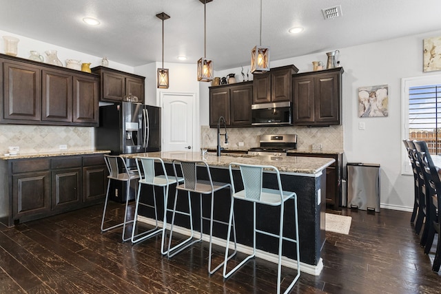 1753 Rio Penasco Rd, Fort Worth, TX 76052 - kitchen with appliances with stainless steel finishes, a kitchen breakfast bar, dark wood-type flooring, decorative backsplash, and recessed lighting