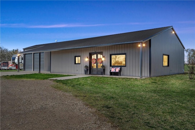 rear view of house with a lawn, dirt driveway, board and batten siding, metal roof, and a garage