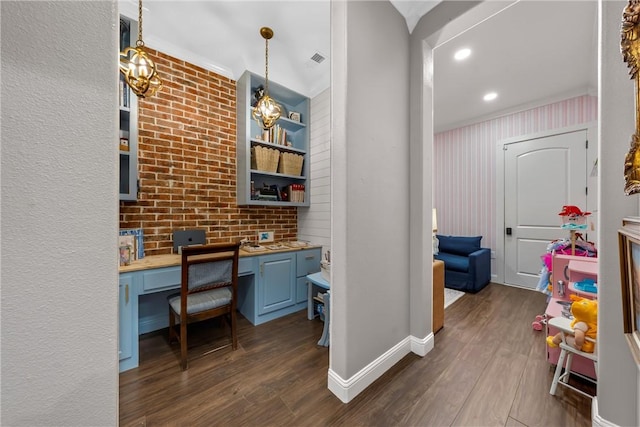 office space featuring baseboards, brick wall, built in study area, dark wood finished floors, and a chandelier
