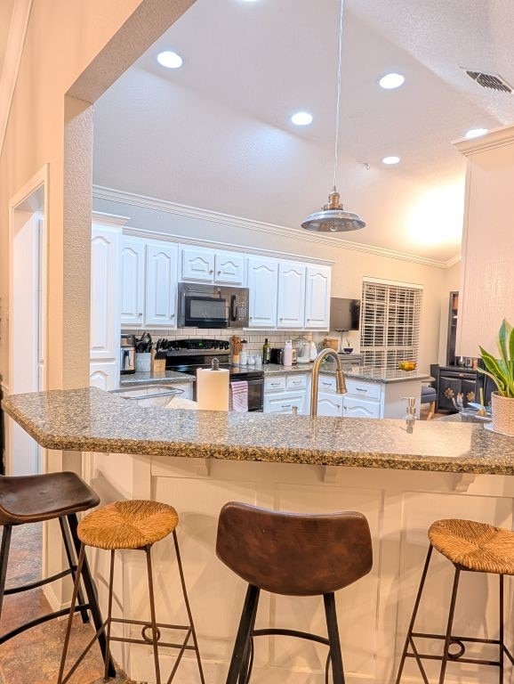 kitchen featuring visible vents, ornamental molding, black appliances, a kitchen breakfast bar, and tasteful backsplash