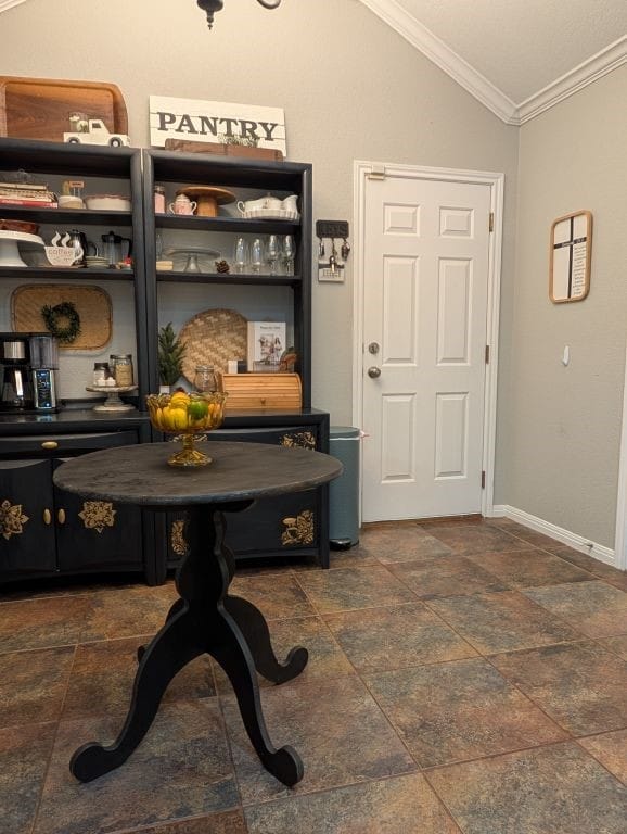 interior space with stone finish floor, baseboards, lofted ceiling, and ornamental molding