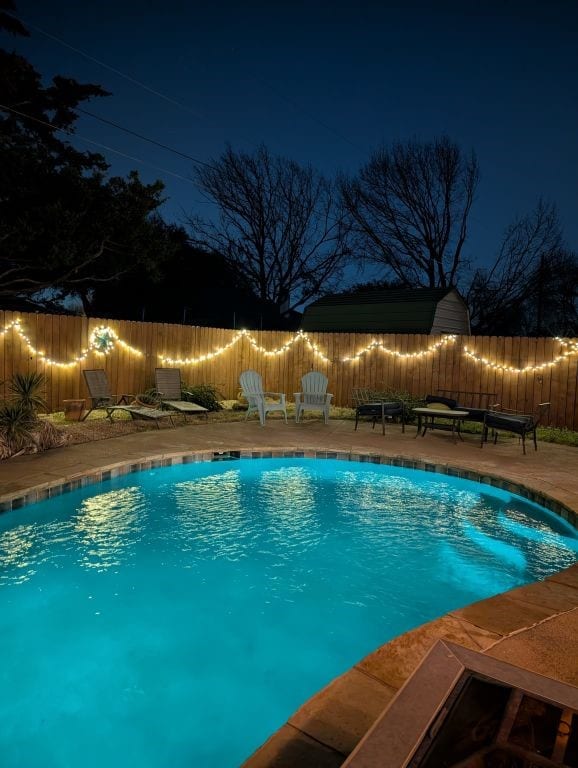 pool at twilight featuring a fenced in pool, a fenced backyard, and a patio area