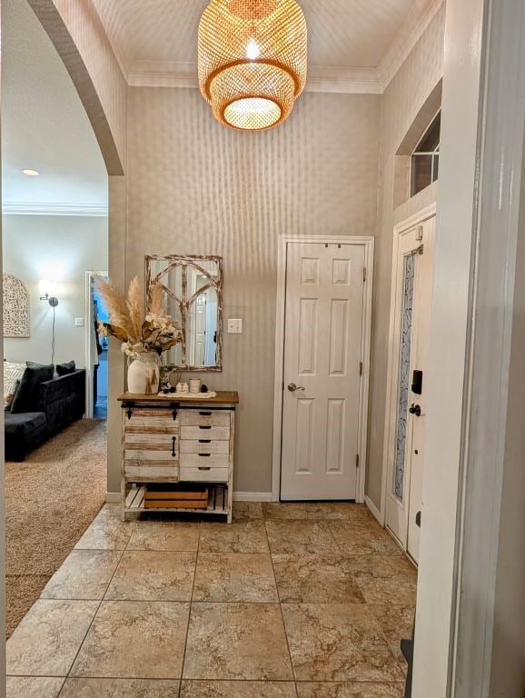 carpeted entryway featuring arched walkways, wallpapered walls, crown molding, and baseboards