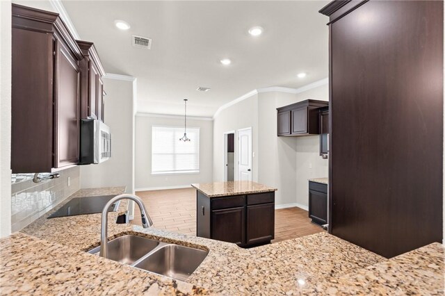 kitchen featuring decorative backsplash, visible vents, dark brown cabinets, a sink, and light stone counters