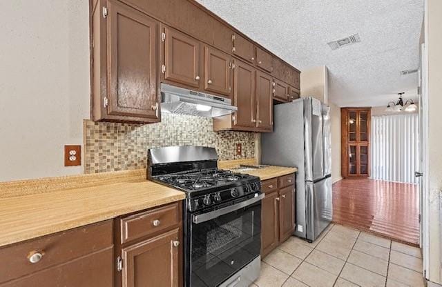 1901 Ruidoso Dr, Waco, TX 76712 - kitchen with black range with gas cooktop, under cabinet range hood, freestanding refrigerator, light countertops, and a textured ceiling