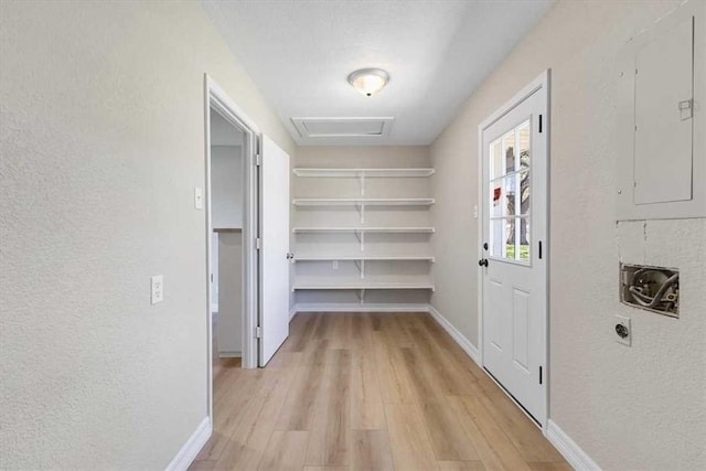 hallway with baseboards, attic access, electric panel, a textured wall, and light wood-type flooring