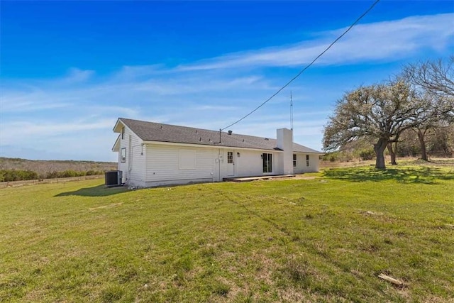 rear view of property featuring central air condition unit and a lawn