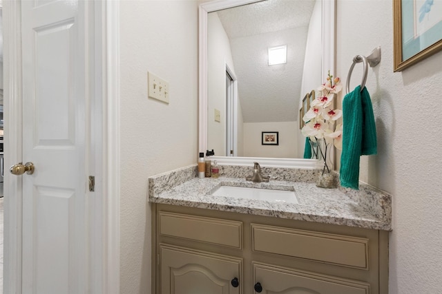 bathroom featuring a textured ceiling, vanity, and a textured wall