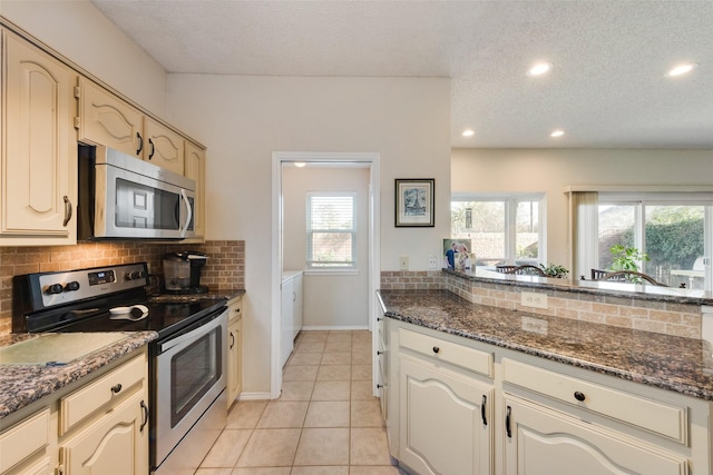 kitchen featuring dark stone countertops, light tile patterned floors, tasteful backsplash, and appliances with stainless steel finishes