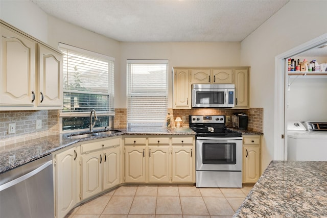 kitchen with light tile patterned flooring, a sink, stainless steel appliances, washer and dryer, and cream cabinets