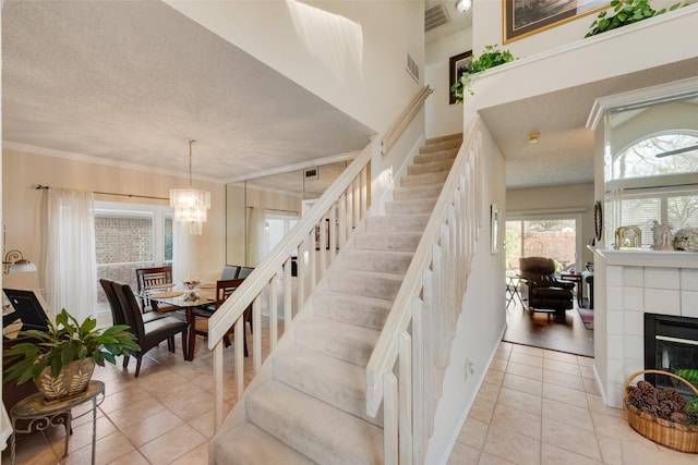 staircase featuring tile patterned flooring, visible vents, a tiled fireplace, and crown molding