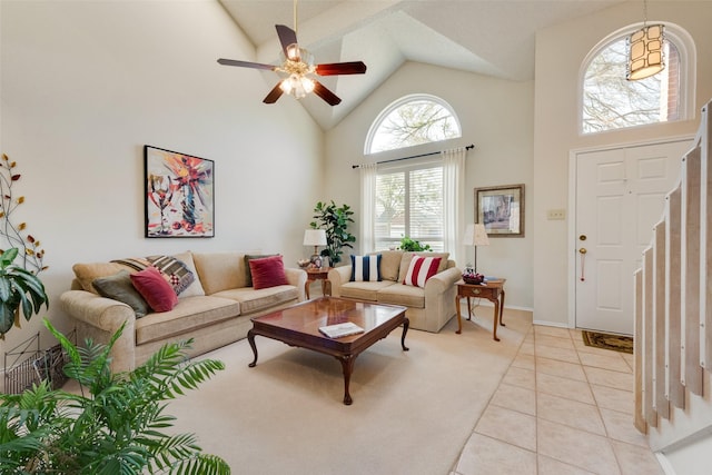 living room featuring baseboards, high vaulted ceiling, light tile patterned flooring, ceiling fan, and stairs
