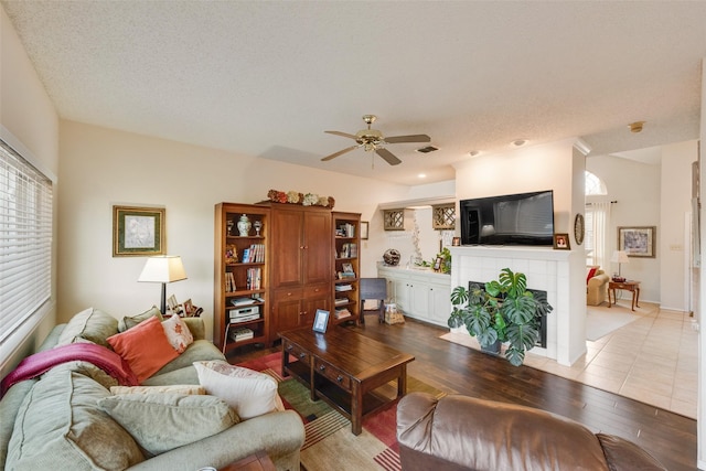living area featuring a fireplace, a textured ceiling, a ceiling fan, and wood finished floors