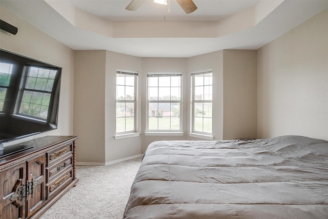 carpeted bedroom with a raised ceiling, a ceiling fan, and baseboards