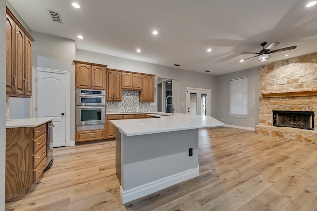 kitchen with a sink, a center island with sink, open floor plan, stainless steel double oven, and brown cabinetry
