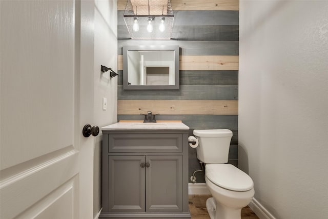 half bathroom with baseboards, wood finished floors, vanity, and toilet