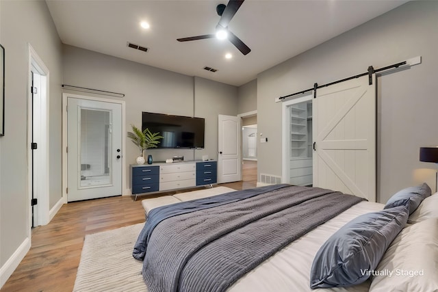 bedroom with light wood finished floors, baseboards, visible vents, and a barn door