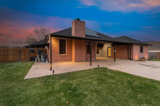 back of house with a fenced backyard, a chimney, brick siding, and solar panels