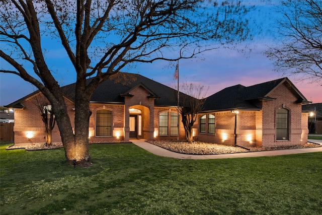 ranch-style house featuring a shingled roof, brick siding, and a yard