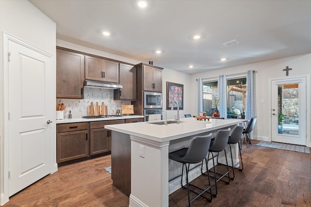 113 Glenwood Dr, Oak Point, TX 75068 - kitchen featuring under cabinet range hood, wood finished floors, a center island with sink, stainless steel appliances, and recessed lighting