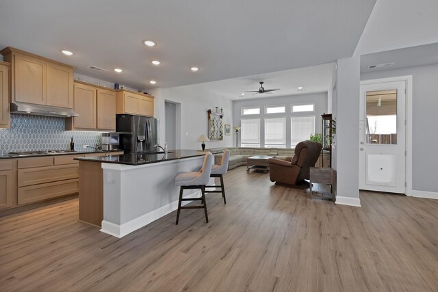 kitchen with light wood-type flooring, light brown cabinetry, backsplash, dark countertops, and appliances with stainless steel finishes