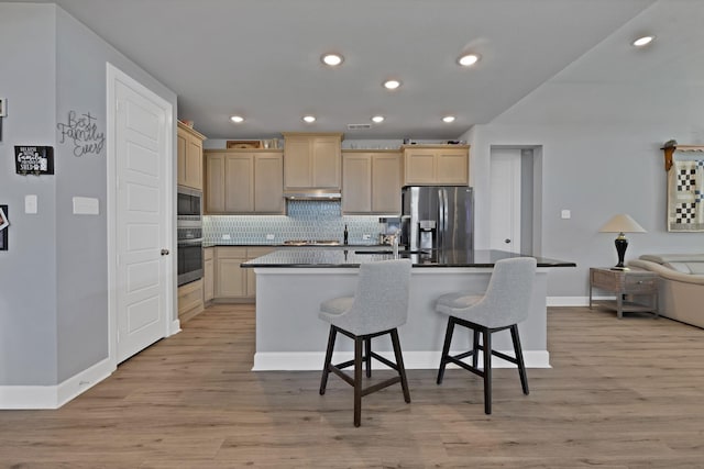 kitchen featuring light wood finished floors, under cabinet range hood, decorative backsplash, baseboards, and appliances with stainless steel finishes