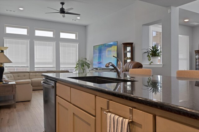kitchen featuring dark stone counters, stainless steel dishwasher, a sink, open floor plan, and a ceiling fan