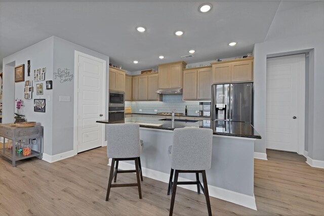 kitchen featuring light wood finished floors, stainless steel appliances, a kitchen breakfast bar, light brown cabinetry, and baseboards