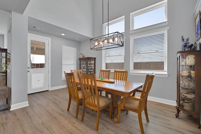 dining area featuring light wood-style flooring, a chandelier, visible vents, baseboards, and a high ceiling
