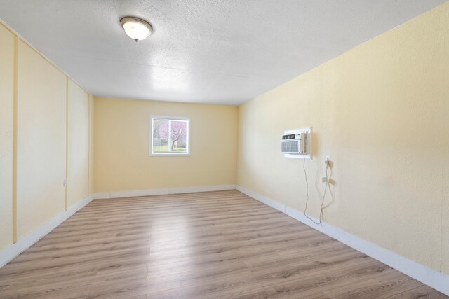 7918 Racine Dr, Dallas, TX 75232 - empty room featuring an AC wall unit, light wood-style flooring, baseboards, and a textured ceiling
